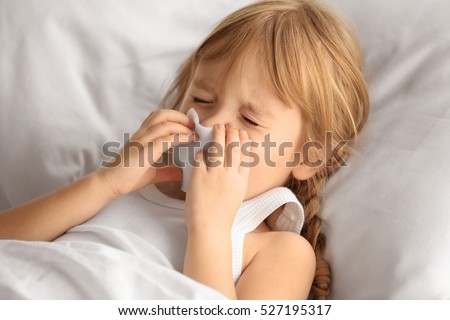 Small sick girl blowing her nose in bed