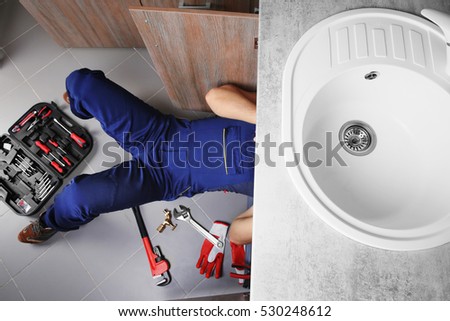 Male plumber repairing sink pipes in kitchen, top view