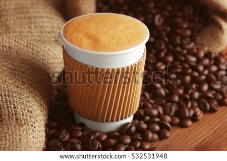 Cup of coffee with roasted beans on wooden table closeup
