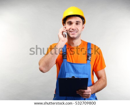Handsome warehouse worker talking by mobile phone while holding clipboard, on light background