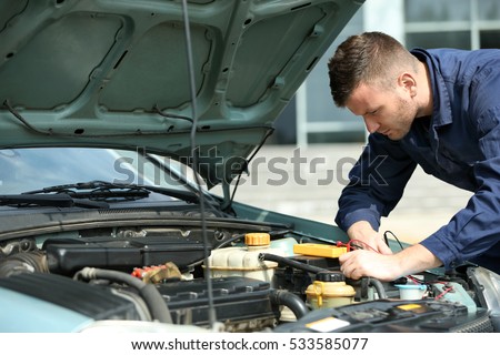Mechanic with scan tool diagnosing car in open hood. Closeup
