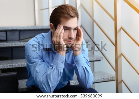 Tired office worker sitting on stairs indoors