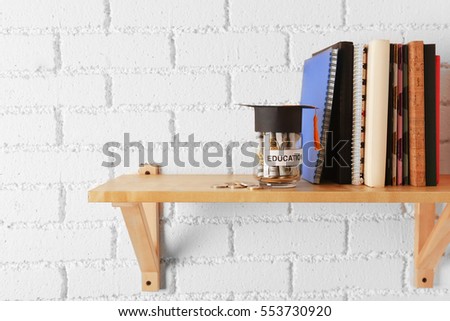 Glass jar with money for education, books and notepads on wooden shelf