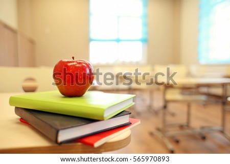 Stack of books and apple on desk at classroom