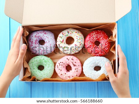 Female hands holding box with colorful donuts on blue wooden background