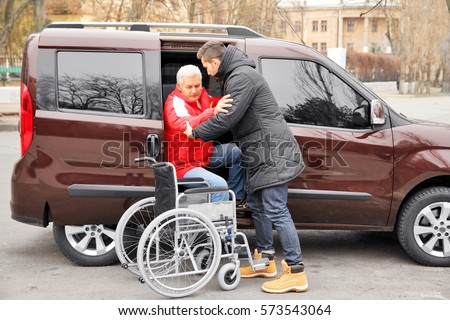 Young man helping handicapped man to sit in wheelchair