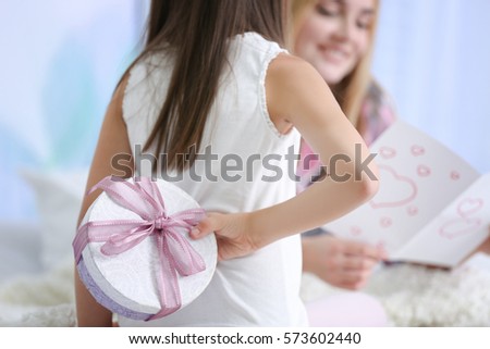 Cute little girl hiding present for her mother behind back, close up. Mother\'s day concept