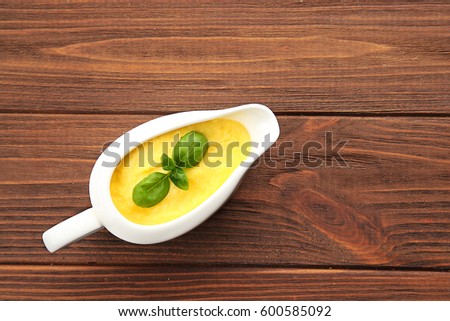 Gravy boat with tasty cheese sauce on wooden background