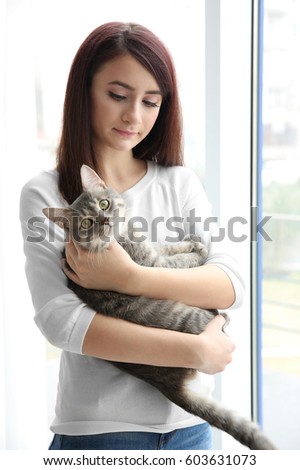 Beautiful young woman with cute cat near window at home