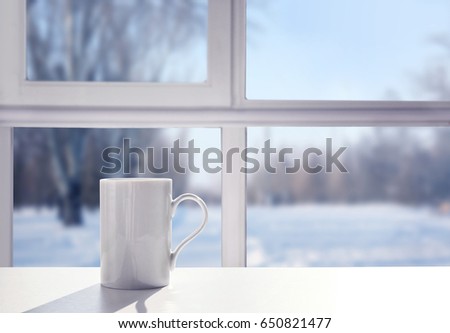 Cup of aromatic tea on windowsill. View of snowy forest from window