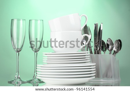 Clean plates, glasses, cups and cutlery on green background