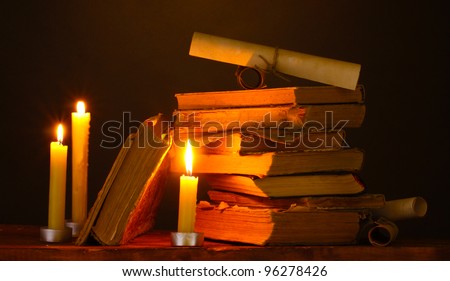 Pile of old books with candle and scroll in dark