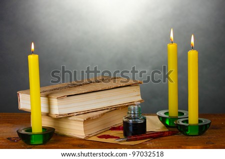 old books, scrolls, ink pen inkwell and candles on wooden table on grey background