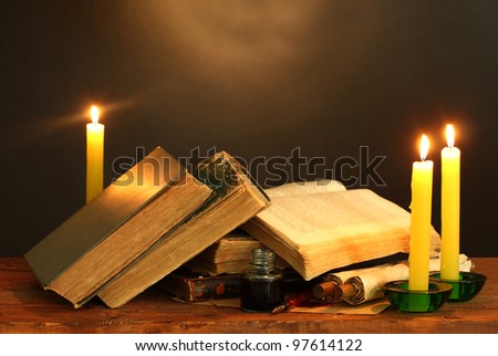 old books, scrolls, ink pen inkwell and candles on wooden table on brown background