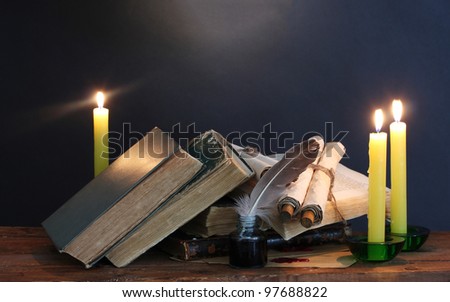 old books, scrolls, feather pen inkwell and candles on wooden table on blue background