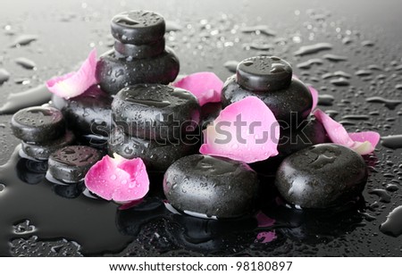 Spa stones with drops and rose petals on grey background