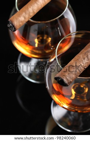 two glasses of brandy and cigars on black background