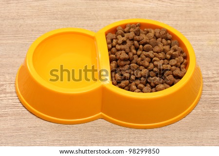 dry cat food and water in yellow bowl on wooden background