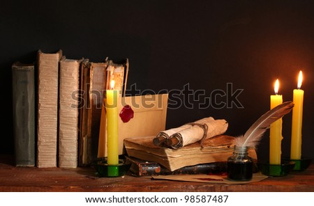 old books, scrolls, feather pen inkwell and candles on wooden table on brown background