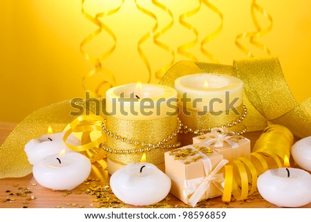 Beautiful candles, gifts and decor on wooden table on yellow background