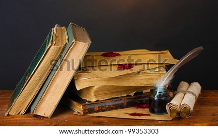 old books, scrolls, feather pen and inkwell on wooden table on brown background