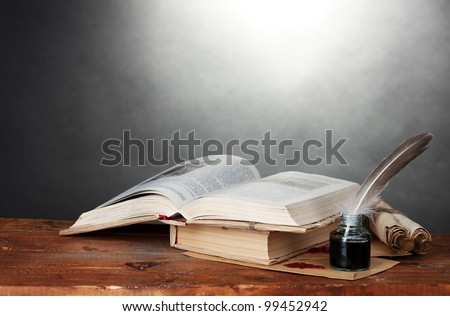 old books, scrolls, feather pen and inkwell on wooden table on grey background
