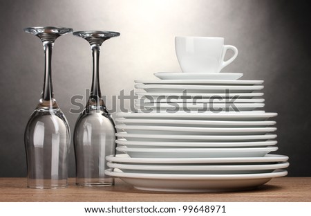 Clean plates, glasses and cup on wooden table on grey background
