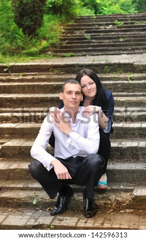 The young man and woman embracing in   park sitting on   background of an old staircase.