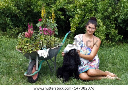 Woman with dog in garden and wheelbarrow with flowers