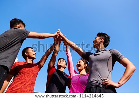 team of asian young adult sportsmen and sportswoman putting hands together to show unity and teamwork spirit.