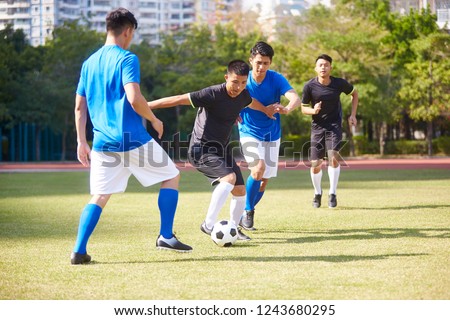 a group of young asian soccer football player playing on outdoor court.