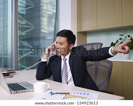asian businessman talking on phone in office, looking angry.