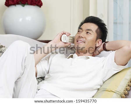 asian man lying on couch talking on phone.