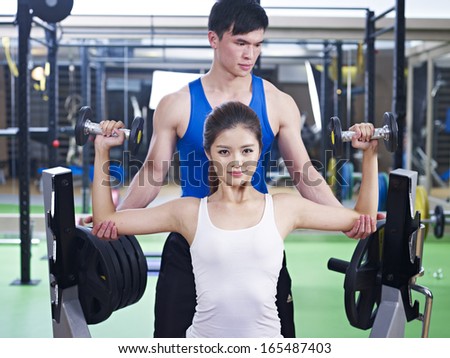 young woman doing body building exercise with help from trainer.