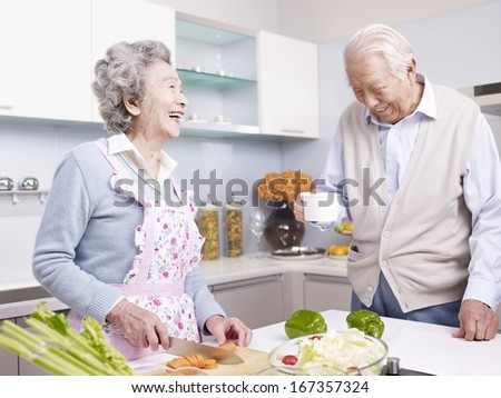 senior asian couple talking and laughing in kitchen.