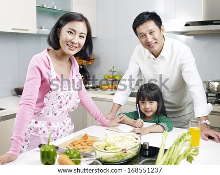 asian family of three smiling in kitchen, focus on father and child.