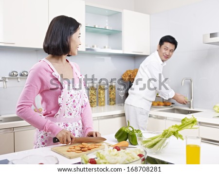 asian couple preparing meal together in kitchen.