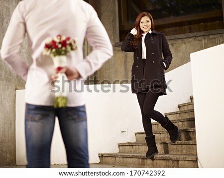 asian young man waiting by the steps with flowers behind back for his girlfriend.