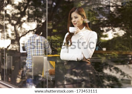 young woman standing in front of windows drinking coffee in cafe.