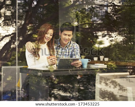 young couple sitting next to windows looking at tablet computer in cafe.
