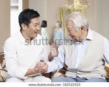 asian father and adult son chatting on couch
