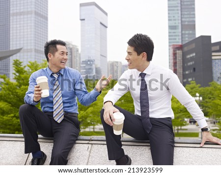 two asian business executives talking in city park while taking a coffee break.