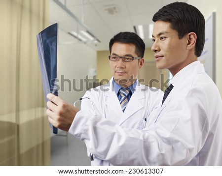 two asian doctors looking at x-ray film in consultation room.