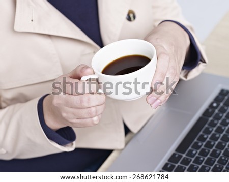 female office worker sitting in front of laptop computer with a cup of coffee in hand, high angle view.