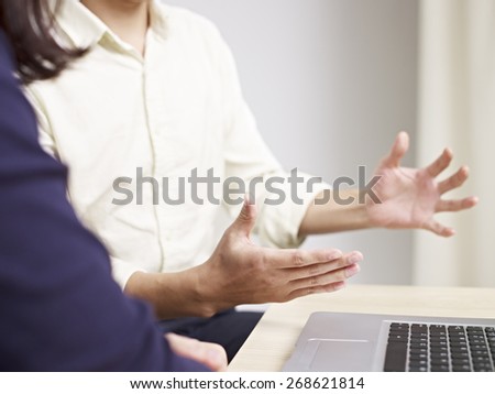 male office worker using hand sign while talking to female colleague in office.