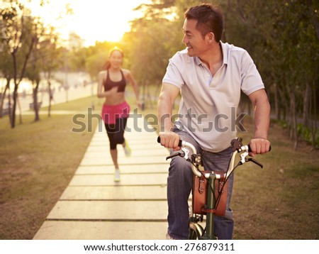 young asian couple running, riding bike outdoors in park at sunset, fitness, sport and exercise, healthy life and lifestyle concept.