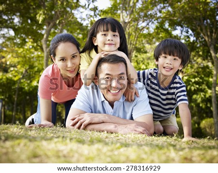happy asian family with two children taking a family photo outdoors in a park.