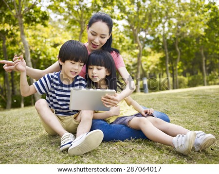 asian mother and two children using tablet computer outdoors.