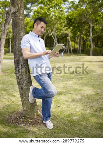 asian man in casual wear using tablet computer outdoors in park.