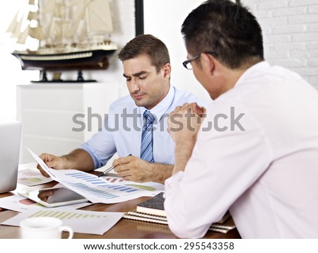 asian and caucasian business executives reviewing and discussing business performance in office of a multinational company.